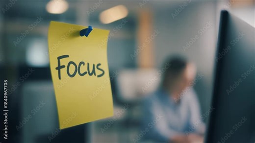 Yellow Sticky Note with the Word Focus Written in Black Ink Attached to a Glass Wall in a Modern Office Environment