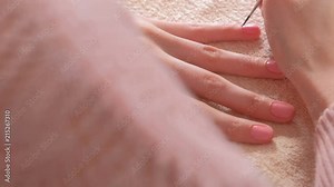 Woman puts second coat of pink shellac on her nails with small tassel. Close-up hands.