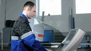 Mechanical technician programming punching the machine CNC. A man enters the data carefully to control panel. Metal is processed on a background
