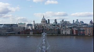 Forward fly above modern designed Millennium Footbridge across River Thames. Heading towards Saint Pauls Cathedral. Domed building on Ludgate Hill. London, UK