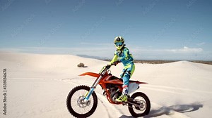 Professional dirt biker riding on sand dunes doing stunts. Motorcyclist riding his bike across desert doing wheelie.
