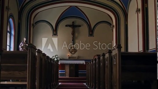 Low angle tilt up view of interior of traditional church with wooden benches and long aisle leading to altar with crucifix on wall
