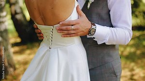 A man gently runs his hand down the back of his beloved. A girl in a white dress. Close - up of the hand.