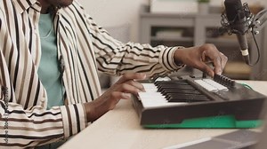 Lockdown of unrecognizable African-American man sitting at m-audio keystation at home and playing synthesizer. Music creation at home studio