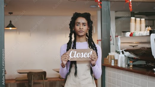 African american female Barista shows closed sign in cafe while colleagues and customer wait in background during midday work hours