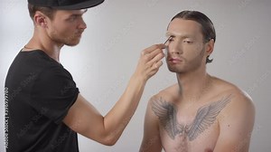 Medium shot of professional male make-up artist using spoolie brush to comb through male models eyebrows