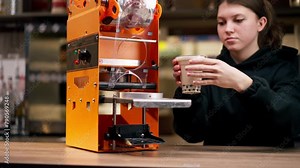 close-up of an orange machine for packaging drinks with plastic on bar counter hands setting up the machine