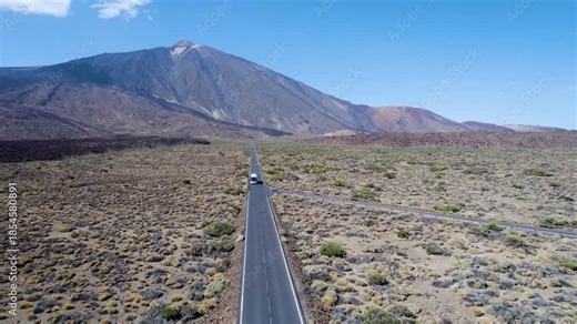 Drone flying over a long road through volcanic terrain, with a bus in motion and a prominent volcano in the background in Tenerife, Spain, suitable for travel and destination establishing shots.