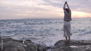 View from the back, beautiful woman dancing in the evening on a rock by the sea Stock Video