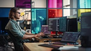 Male Backend Software Developer Writes Code on Desktop Computer With Two Monitors in Coworking Office Space. Caucasian Man Creating Database for Online e-Commerce Store or New Social Network.