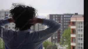 Hispanic curly hair business woman styling curly hair on city balcony view. Captured in a moment of personal care amidst urban life.