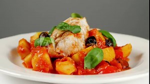 Traditionally prepared cod in Spanish. Served in tomato sauce with boiled potatoes, olives and basil. Front view. Food presentation. Turning the platter.