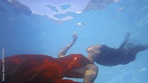 Underwater footage of a young woman in red dress swimming close to the surface