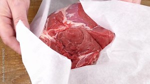 putting a raw beef clod on a white wrapping paper onto a woooden cutting board closeup slow motion