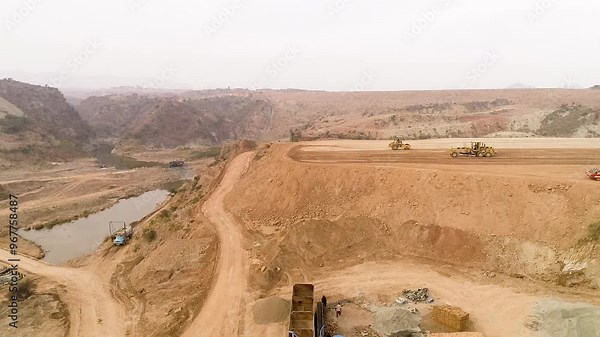 Excavator digging sand in river and loading dump truck, two tipper driving loaded on sandbank, mad floating on water flow