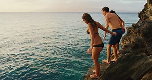Friends cliff jumping into the ocean at sunset