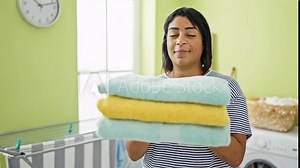 A smiling middle-aged hispanic woman holds folded towels in a bright green laundry room, imbuing a sense of domestic contentment.