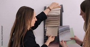 Interior designers select fabrics, paint from mood board for home renovation, discussing color scheme details. Meticulous interior design process, expertise in creating stylish, harmonious spaces.