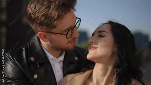 Slow motion. Close-up. A man with glasses hugs a beautiful woman and they look at each other. They then both look at the camera