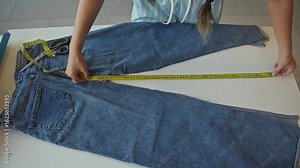 Seamstress uses measuring tape to determine leg length of pair of jeans. This is necessary in order to tailor them to fit and organize them in their sewing workshop.
