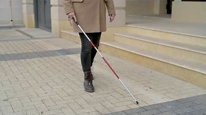 Free stock video - Mid view of a blind woman in brown coat walking with a walking stick in the street