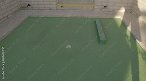 This video shows a golf ball coming out of hole, bouncing off a wall, and rolling into the putting course hole.