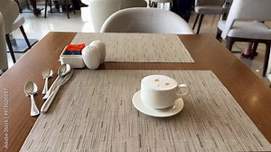 A coffee cup is placed on a saucer, resting on a wooden table. The tableware includes dishware and drinkware, making it a perfect setting for enjoying a hot drink