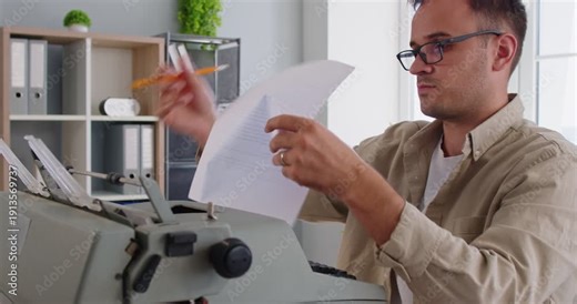 Man typing on old typewriter, writer holding paper from old machine to read text and edit draft of book. Busy author with glasses typing at desk in office, preparation for content publication