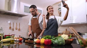 Happy young married couple cooking together in the kitchen. Young couple using smartphone for video call in the kitchen.