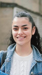 Vertical portrait of a pretty hispanic female student smiling and looking at camera in the high school. Head shot portrait of latin teenager girl standing outdoors at the university campus. Education