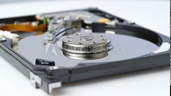 A detailed view of an opened laptop hard disk drive (HDD), revealing its internal components. The shiny, circular platter, the head assembly, and the actuator arm are clearly visible