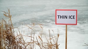 Close-up of a "Thin Ice" warning sign in front of a frozen lake. Stop, danger, warning.