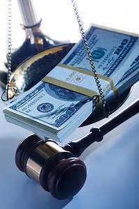 A stack of $100 bills sits on a brass justice scale which sits next...