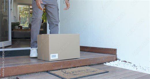 Man is stepping onto porch from ajar glass door, lifting cardboard box and carrying it inside