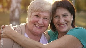Two cheerful elderly ladies hugging on nature