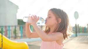 Child playing on playground warm summer day. Little girl have fun. Happy childhood. Drink water plastic bottle