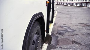 Side view of the white bus with opening door and bus wheel on grey asphalt background. Scene. Close up of passenger bus, opened door flashing light and its wheel, commercial transport wheels concept. Stock Video