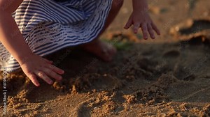 Little girl digging barefoot in the sand on the beach
