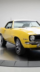 Experience classic American muscle with this 1969 Chevrolet Camaro Z28 coupe in vibrant yellow with crisp white racing stripes and a pristine white vinyl roof. Chrome bumpers, Goodyear tires, and iconic Z28 badges complete the perfect vintage stance. Shot vertical 9:16 in ultra-realistic 4K, handheld POV with soft micro-shake, showcasing every detail: gleaming paint, reflections on chrome, round headlights, sleek side profile, and precise emblems. No music, no narration — just diegetic ASMR soun