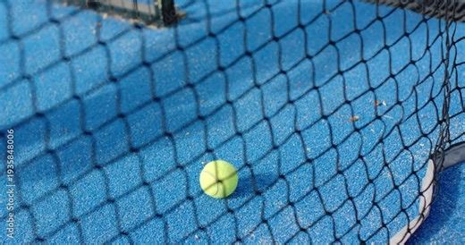 African American woman seeing tennis ball on blue court, reaching through net, picking up ball