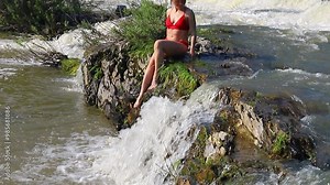Beautiful adult slender woman in a red swimsuit is bathing in a small waterfall.