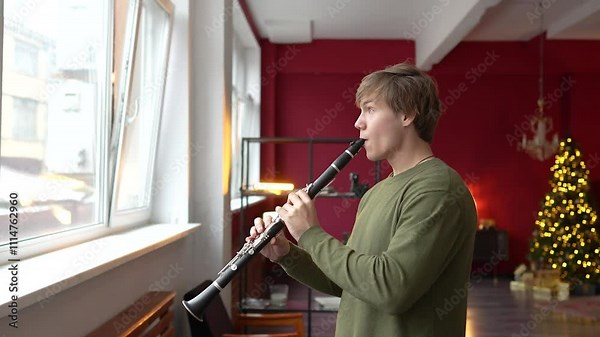 Active man playing clarinet near window in music classroom on Christmas Eve. Male using wind instrument for practice, New Year seasonal rehearsal, prepare for winter performance, musical discipline