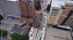 An aerial capturing the demolition of a high-rise building in downtown Youngstown, Ohio. The scene includes a crane in operation, scattered debris, construction vehicles, and adjacent structures,
