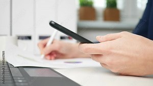 Businesswoman writes in document and uses smartphone. Businesswoman or entrepreneur in home office. Online business, marketing or learning concept. Tax return and business plan. tax declaration