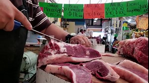 Carnicero con cubrebocas cortando la carne en el mercado