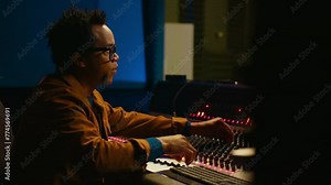 Portrait of professional sound engineer recording tracks and editing tunes by adjusting volume levels with knobs. Producer creating music with mixing console in post production studio. Camera A.