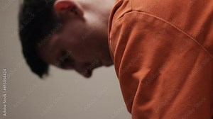 An unhappy criminal, convicted man in prison or jail cell serving sentence. A sad, depressed attractive, handsome man, criminal prisoner, inmate in orange jumpsuit sitting in prison cell.