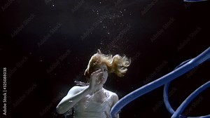 A young slender girl is under water on a dark background in a polluted environment, polyene bags floating around her, in which she is entangled, corrugated pipes.