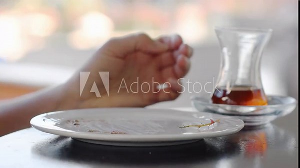 woman using fork scrapes the remains of delicious dessert from white ceramic plate on the table, drinks black Turkish tea from glass cup and leaves, leaving dirty dishes on the table in cafe