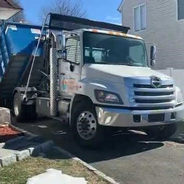 Hino 338 33,000 GVWR Stellar 12-ton Hook Lift Truck Picking Up full 20 Cubic Yard Roll-Off Dumpster